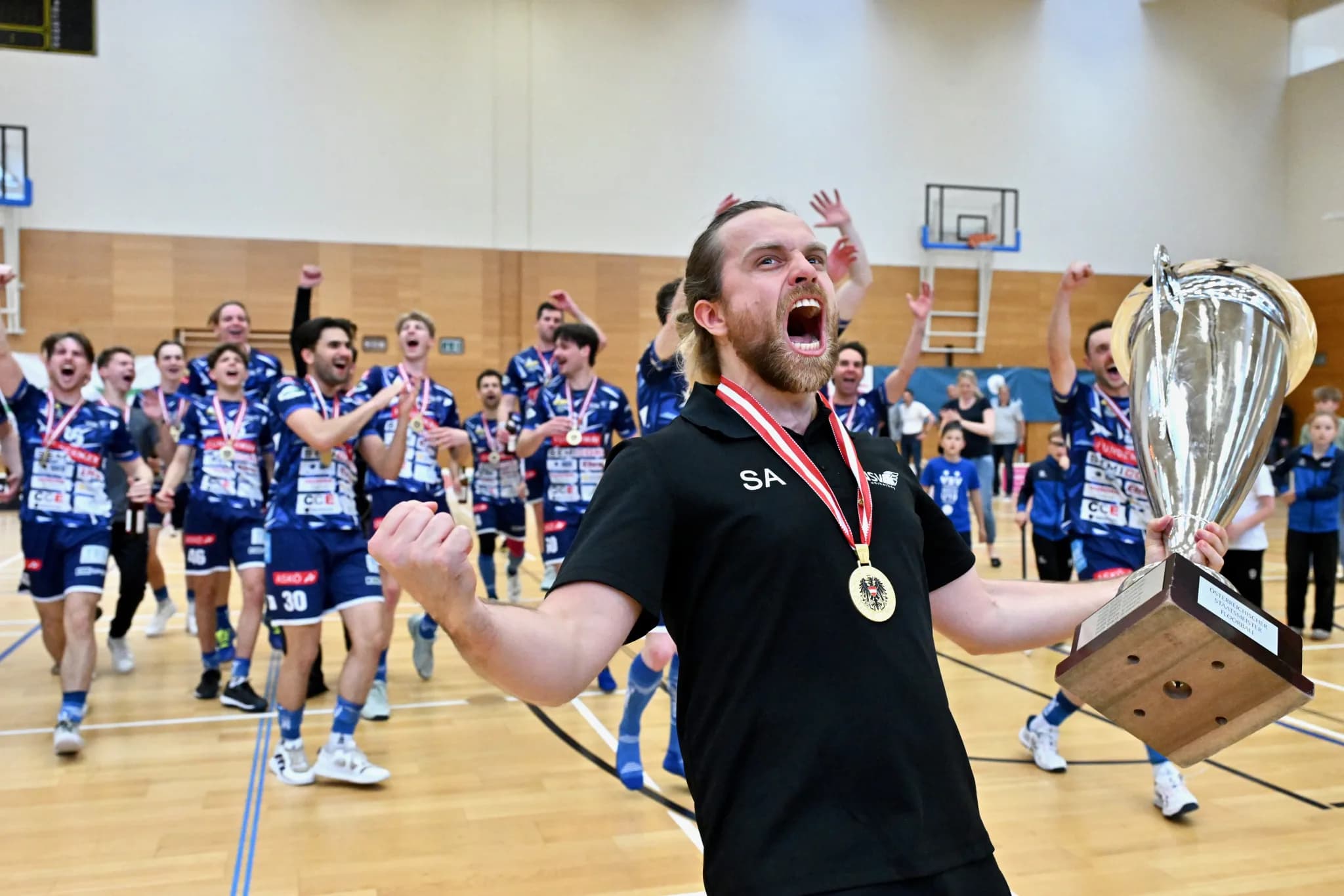 Der Trainer des VSV Unihockey trägt den Meisterpokal, dahinter die jubelnde Mannschaft